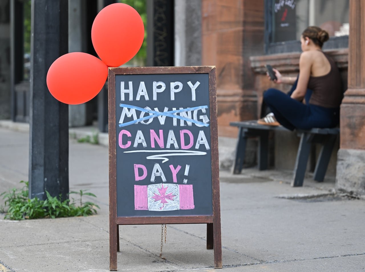 A black chalk sign says, "HAPPY CANADA DAY!" The word "moving" has been crossed out.